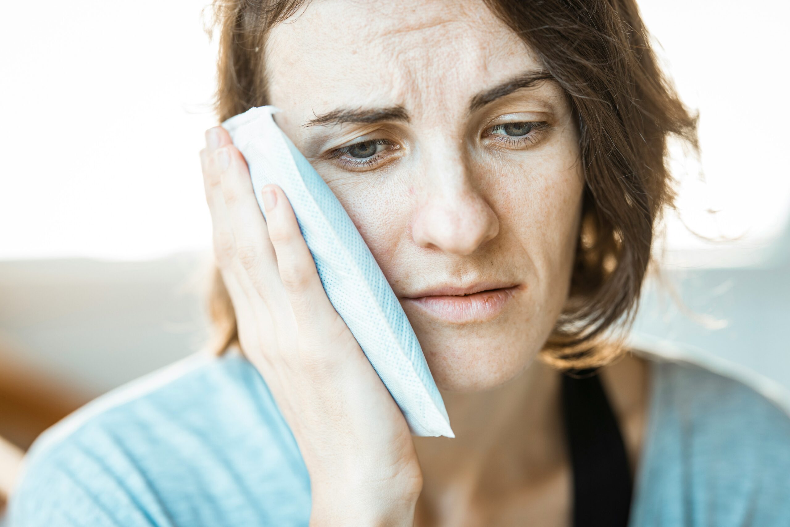 Woman holding an ice pack to her jaw, showing signs of discomfort related to TMJ pain, emphasizing the need for effective jaw pain solutions.