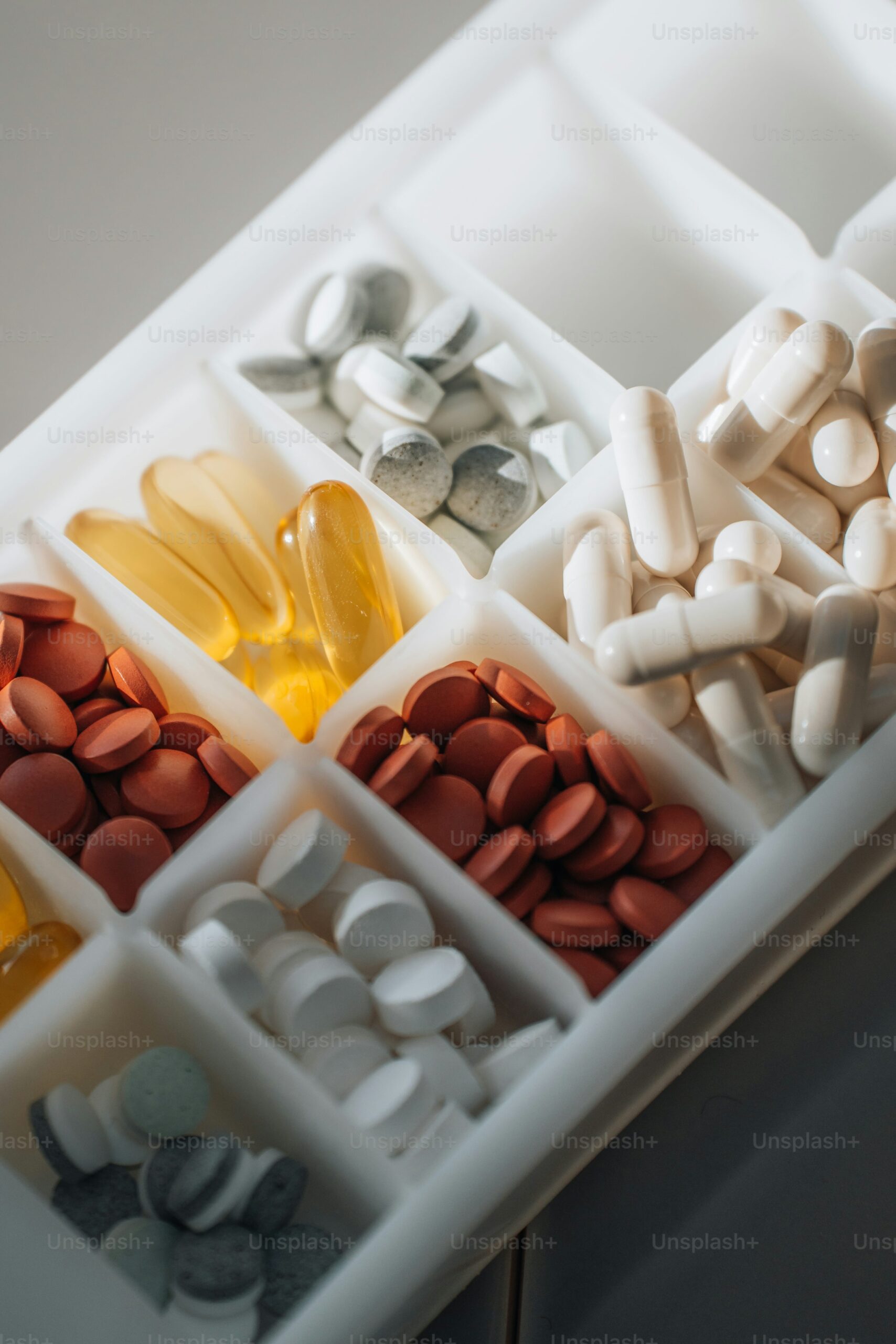 Assorted dietary supplements and vitamins in a compartmentalized organizer, emphasizing nutrition and wellness for health optimization.