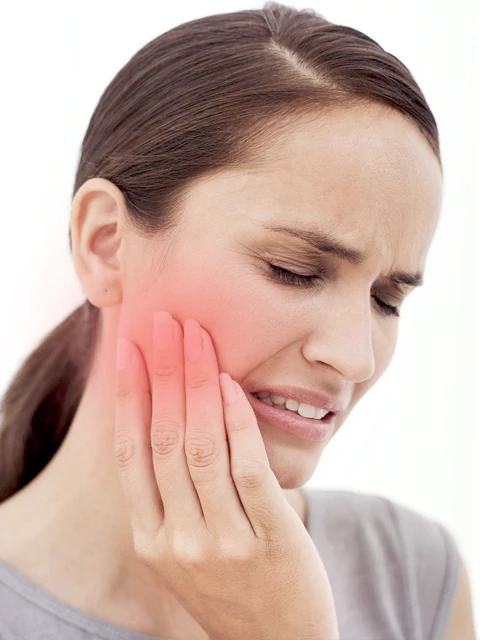 Woman experiencing TMJ pain, holding her jaw in discomfort, highlighting symptoms of temporomandibular joint dysfunction.